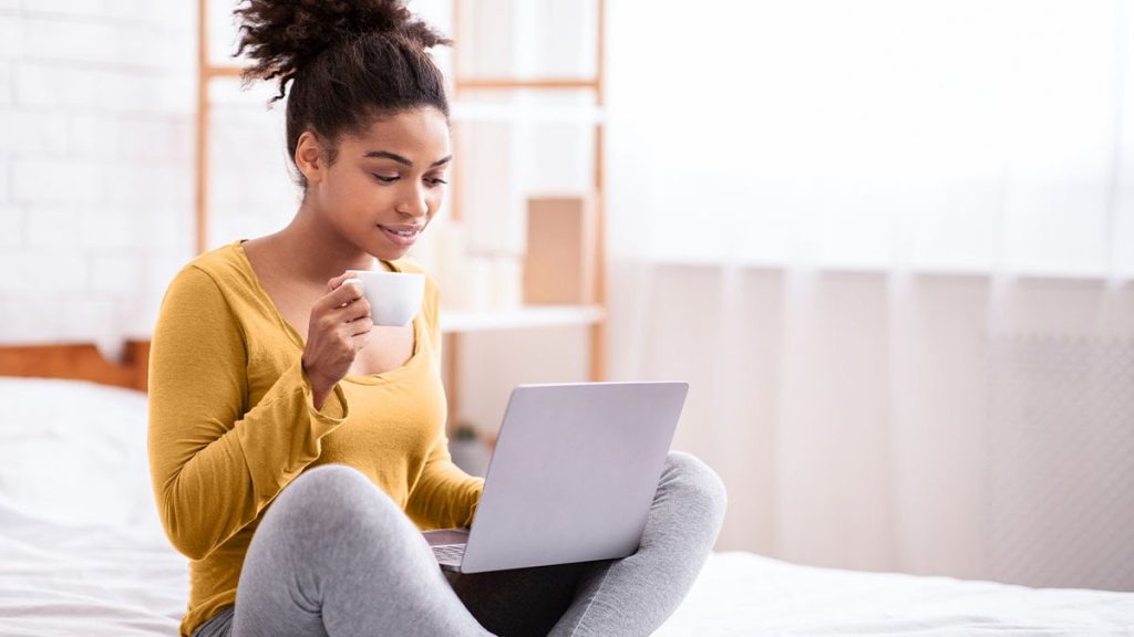 Lady drinking a cup with laptop on her lap